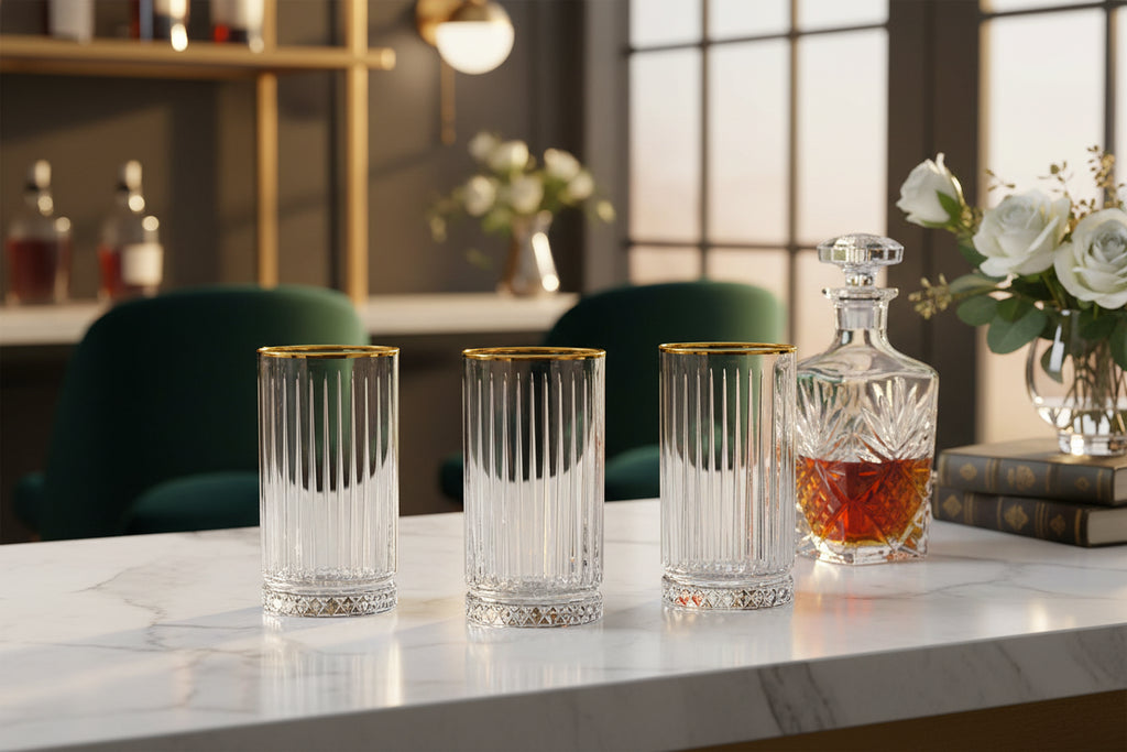 Set of four cylindrical glass tumblers with gold rims on a white background