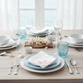 Two white napkins with embroidered blue and red coral designs on a gray surface with starfish and shells.