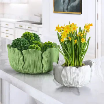 Two decorative planters, one with green plants and the other with yellow flowers, on a white surface.