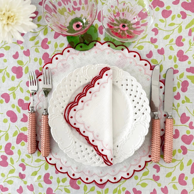 Dinner setting with white plates, pink cutlery, and a floral tablecloth.