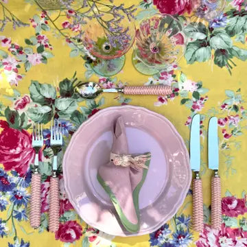 Dinnerware set with floral tablecloth and colorful cutlery on a yellow background