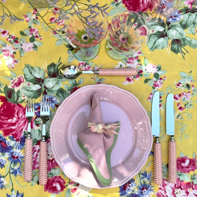 Dinnerware set with floral tablecloth and colorful cutlery on a yellow background